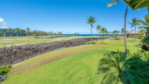 Un campo da golf con vista sull'oceano, palme e un edificio sullo sfondo.