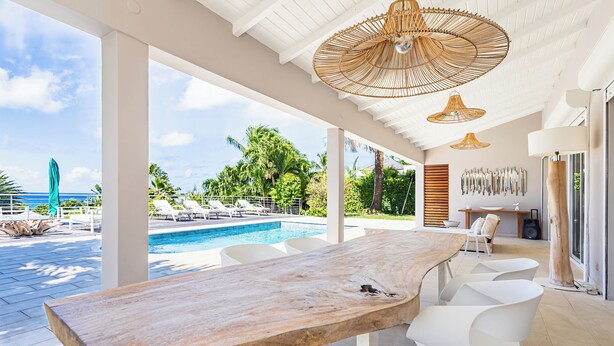 A spacious outdoor area with a pool, white chairs, and a wooden table. - Villa Anse Vinaigri - Beach on foot 👣 (Le Gosier)