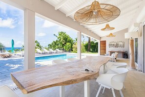 Un vaste espace extérieur doté d’une piscine, de chaises blanches et d’une table en bois.