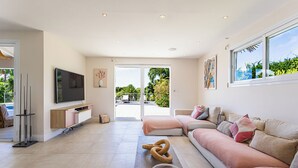 A spacious living room with a large TV, comfortable seating, a glass coffee table, and a view of the outdoors. - Villa Anse Vinaigri - Beach on foot 👣 (Le Gosier)