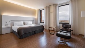 Una habitación de hotel moderna con una cama grande, una mesita, una silla y vistas al paisaje a través de las ventanas.