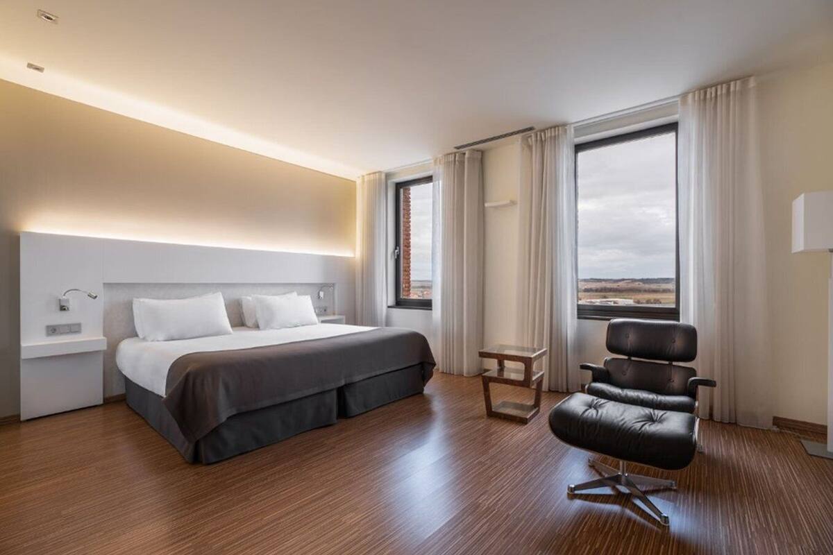 Een moderne hotelkamer met een groot bed, een klein tafeltje, een stoel en uitzicht op het landschap door de ramen.