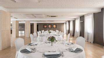 A spacious dining area with round tables set for a formal event, featuring white tablecloths, glassware, and floral centerpieces.