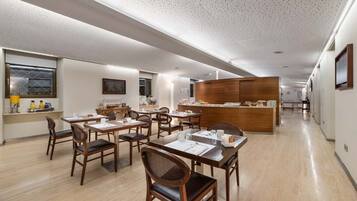 Un comedor moderno de hotel con mesas y sillas de madera, una estación de buffet central y un largo pasillo con suelo pulido.