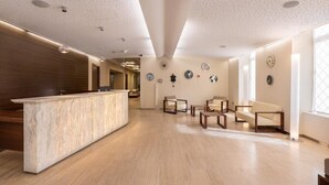 Un área de recepción moderna con una barra de mármol, suelo de madera y una zona de estar con sillas y mesas.