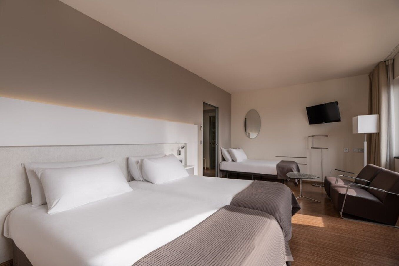 Et hotelværelse med to senge, et skrivebord, en stol, et fjernsyn og et spejl.
