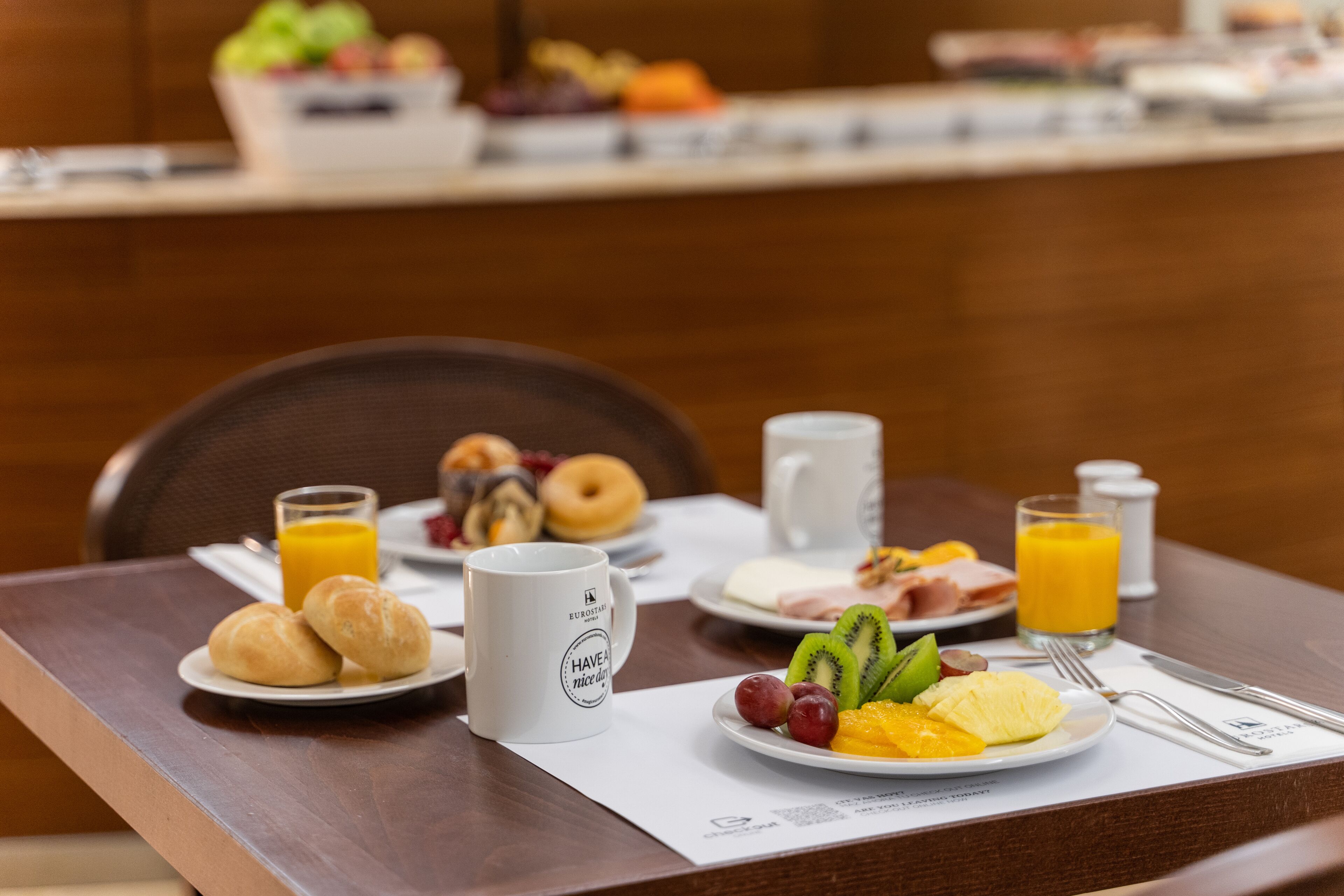 A breakfast table with croissants, a mug, a plate with fruit, and juice glasses.