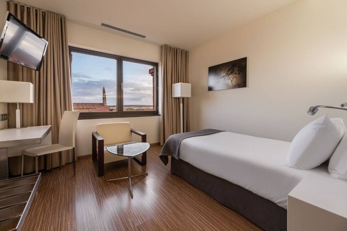 Een hotelkamer met een bed, een bureau, een stoel, een televisie en een raam met uitzicht op een toren.
