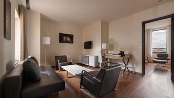A modern hotel room with a sofa, two chairs, a desk, and a TV.