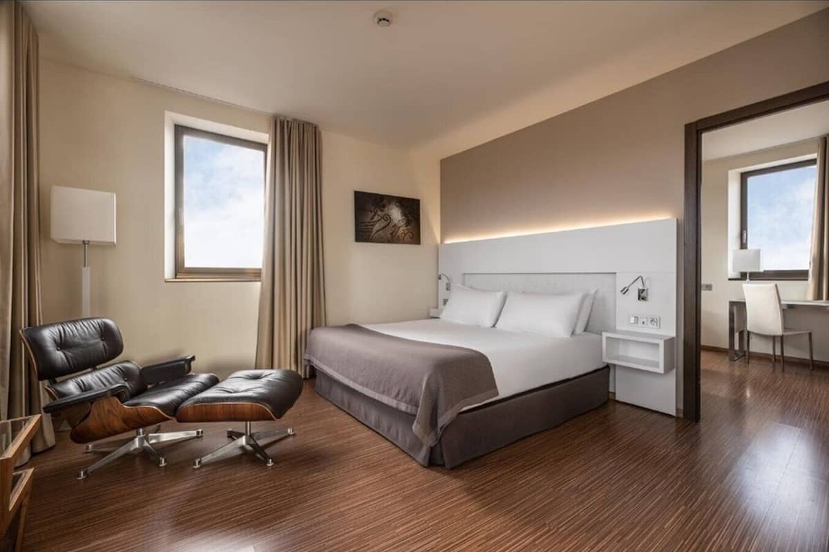 Een moderne hotelkamer met een groot bed, een bureau, een lederen fauteuil en een groot raam.