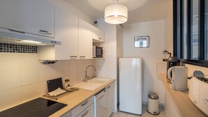 Een moderne keuken met witte kastjes, een zwart inductiekookplaat, een witte koelkast en een koffiezetapparaat.