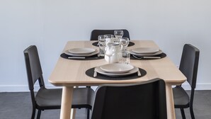 Een eetgedeelte met een tafel voor vier personen, stoelen en een lijst met kunstwerk aan de muur.