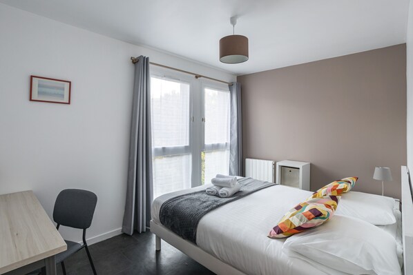 Une chambre à coucher moderne avec un lit, des tables de chevet, un bureau et une chaise.