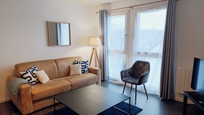 Een moderne woonkamer met een bank, fauteuil, salontafel en een televisie.
