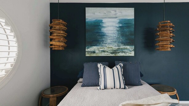Une chambre à coucher comprenant un lit, deux tables de chevet, une fenêtre avec des stores et un tableau accroché au mur.