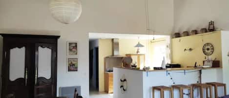 A dining area with a table and chairs, a kitchen with a counter and stools, and a hallway leading to another room.