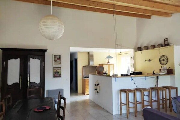 A dining area with a table and chairs, a kitchen with a counter and stools, and a hallway leading to another room.
