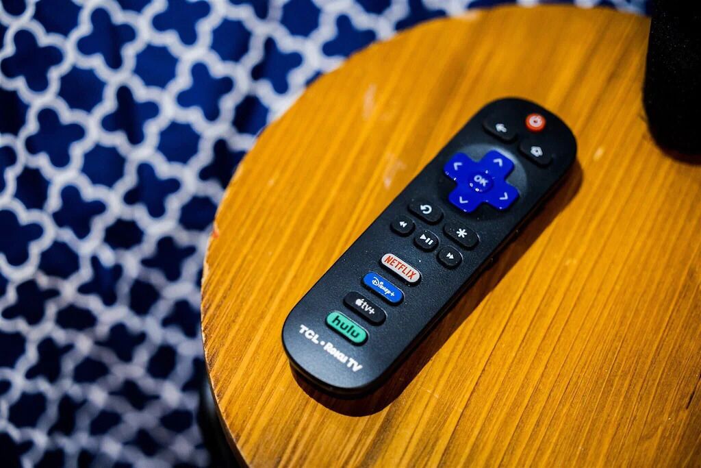 A black remote control with buttons for Netflix, Hulu, and other streaming services on a wooden surface.