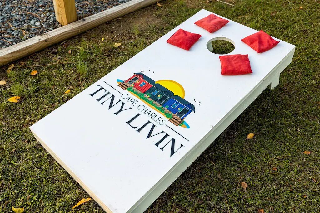 Un juego de mesa blanco sobre césped, con piezas rojas y un logo que dice 'CAPE CHARLES TINY LIVIN'.