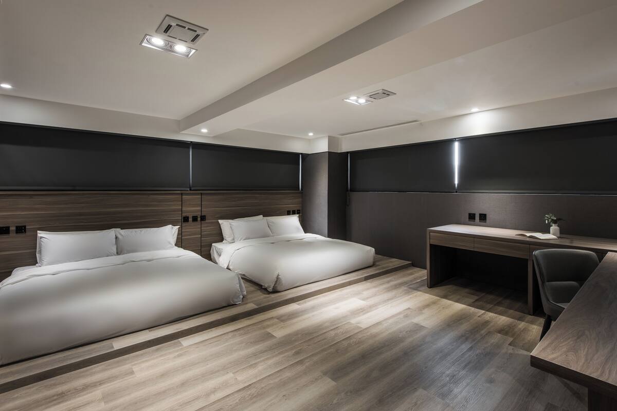 A modern hotel room with two beds, a desk, and a chair.