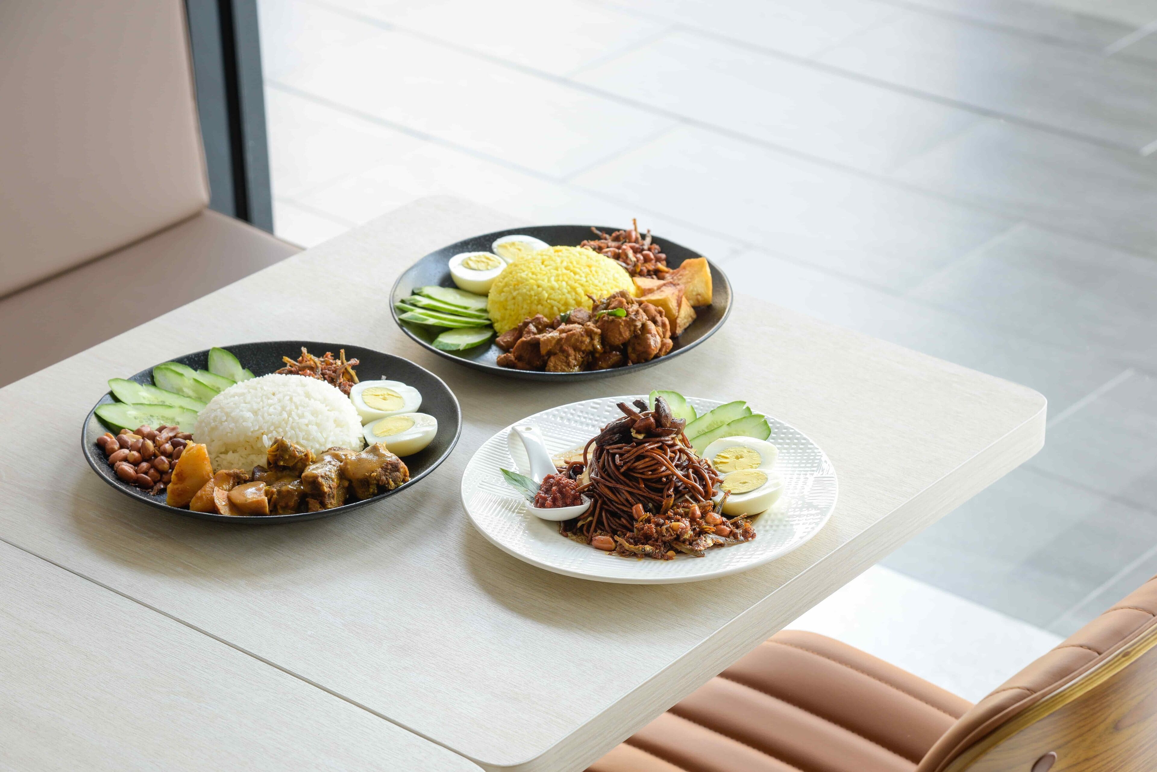 A table with three plates of food, including rice, meat, and vegetables.