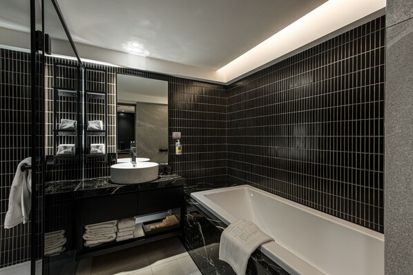 A modern bathroom with a black tiled wall, a white bathtub, and a black vanity with a sink and mirror. - Autumn Willow Hotel (Taichung)