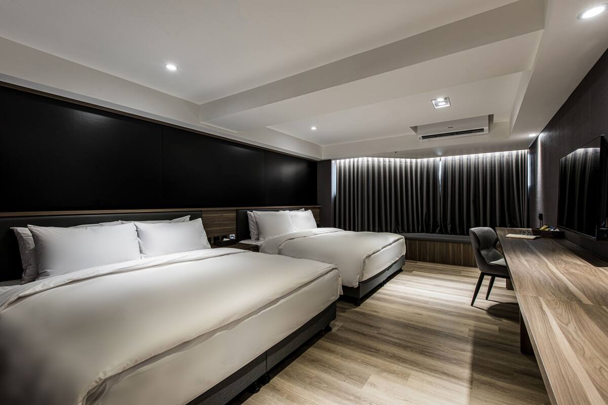 A modern hotel room with two beds, a desk, and a large window with curtains.