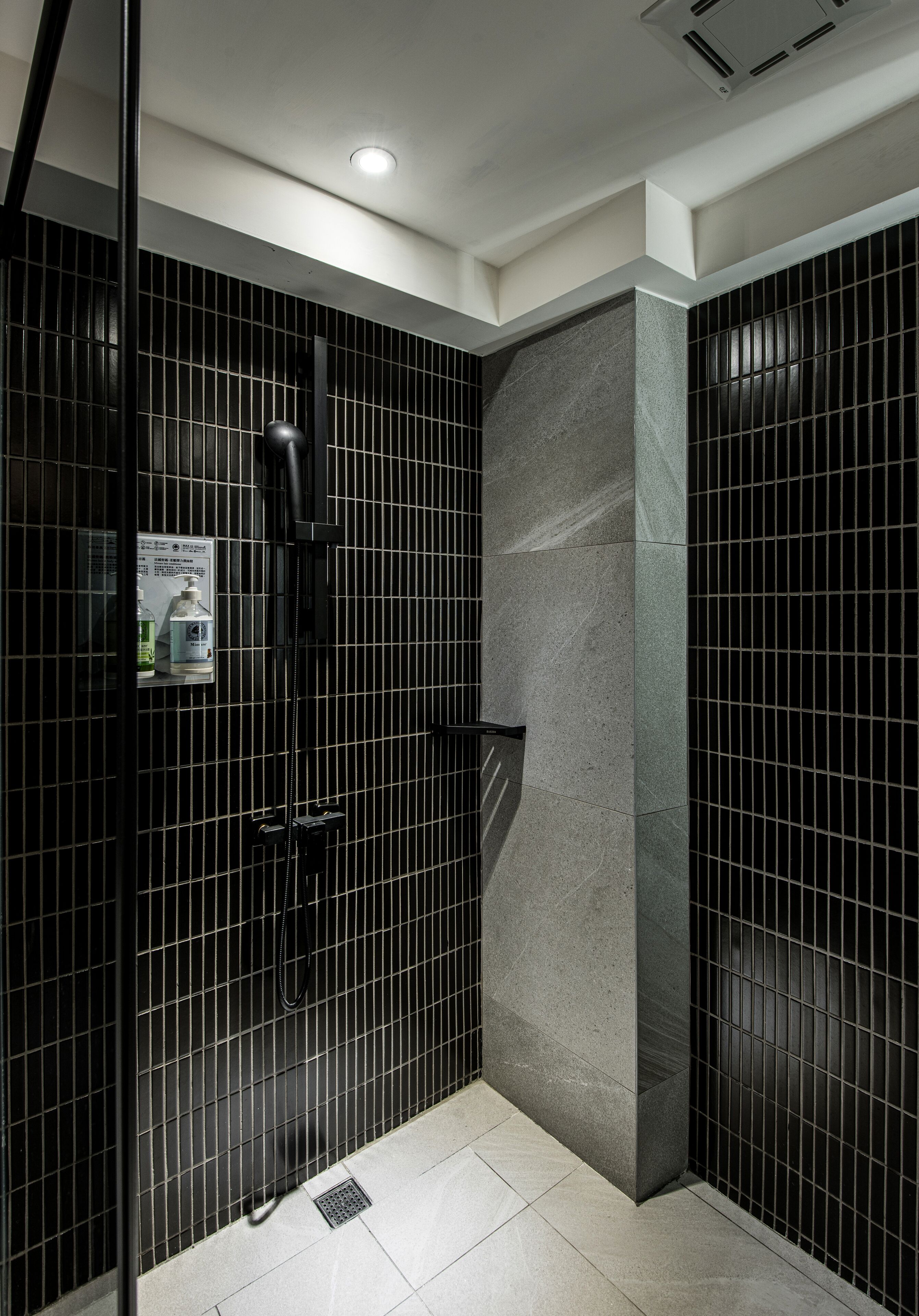 Un baño moderno con paredes cubiertas de azulejos negros, una pared de acento gris y un box de ducha de vidrio.