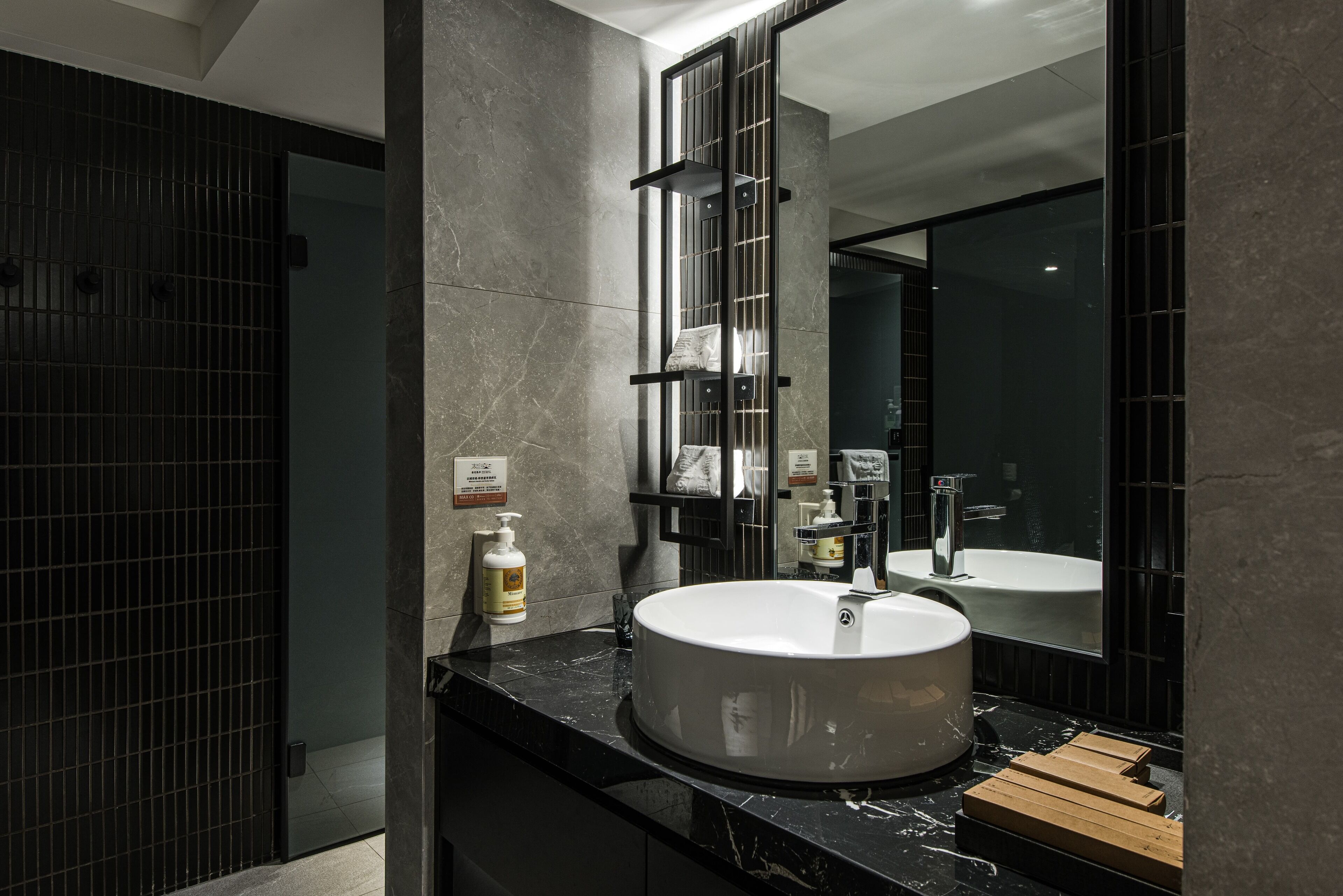 A modern bathroom with a large mirror, a round sink, and a dark tiled wall.