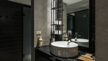 A modern bathroom with a large mirror, a round sink, and a dark tiled wall.