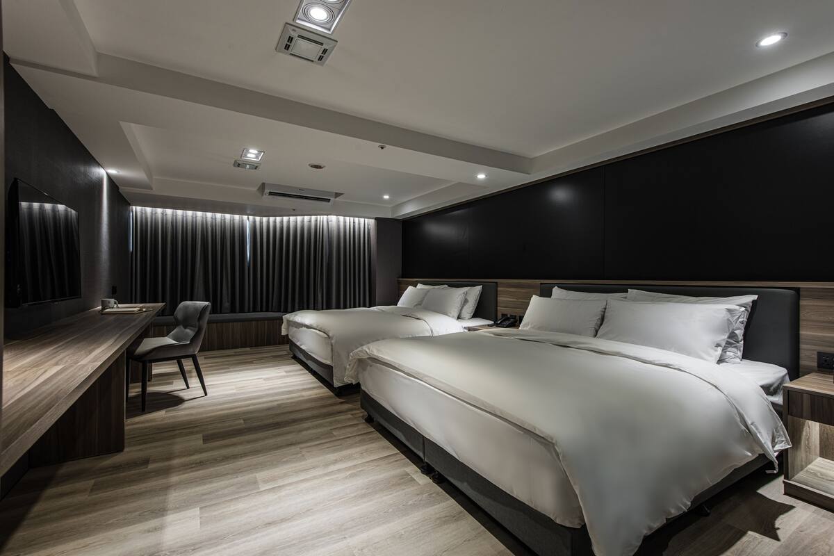 A modern hotel room with two beds, a desk, and a chair.