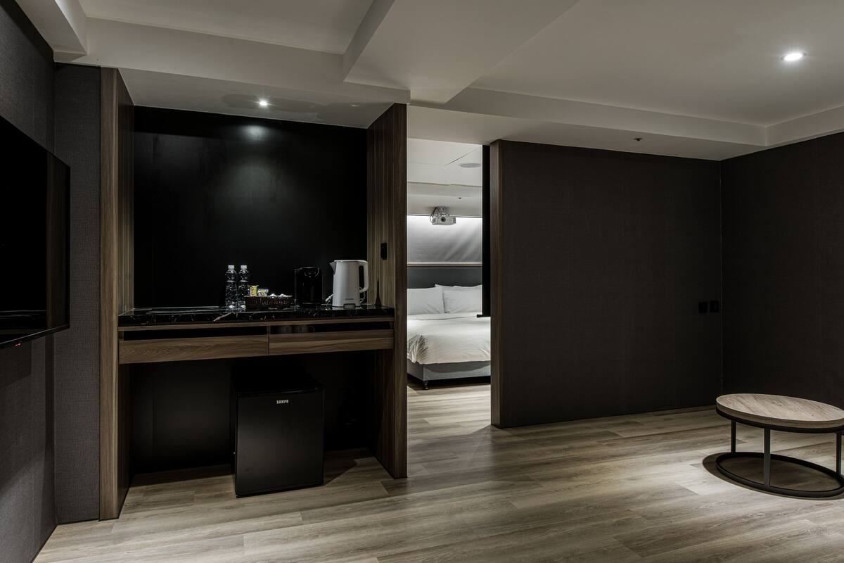 A modern hotel room with a dark wood desk, a bed, and a small round table.