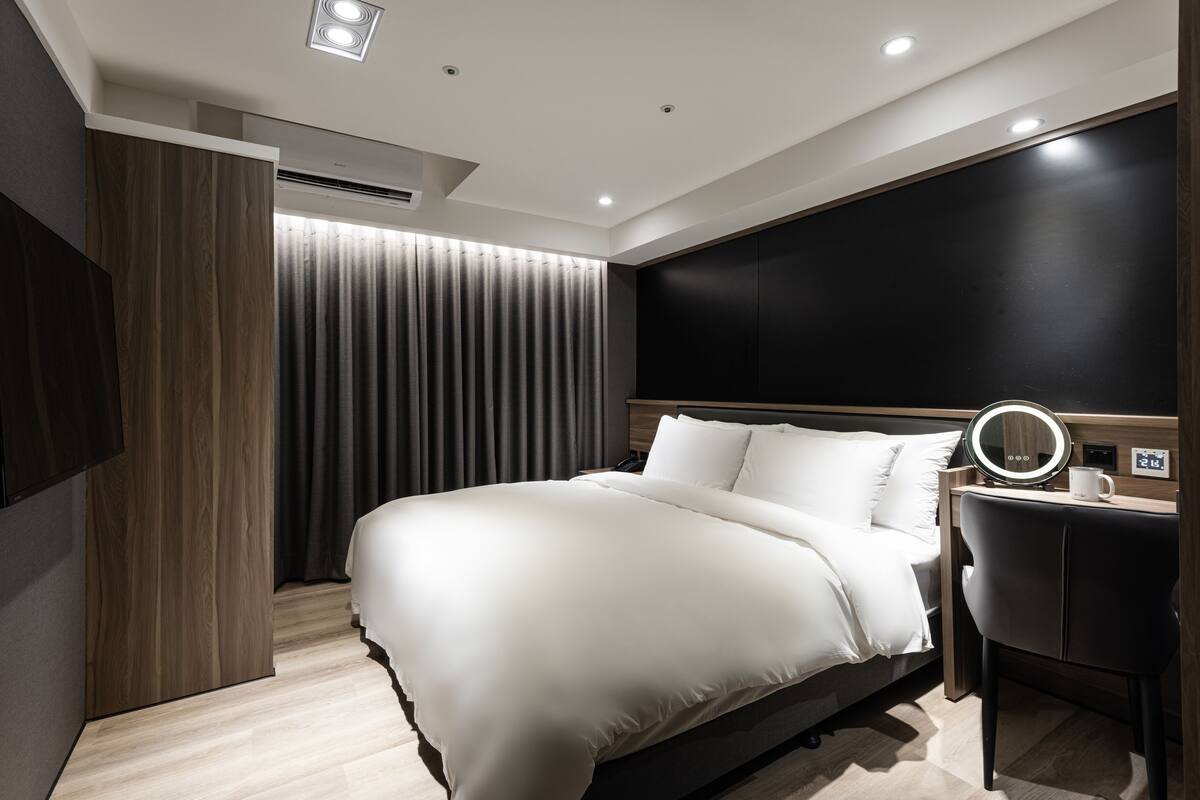 A modern hotel room with a large bed, a desk with a mirror, and a flat-screen TV mounted on the wall.