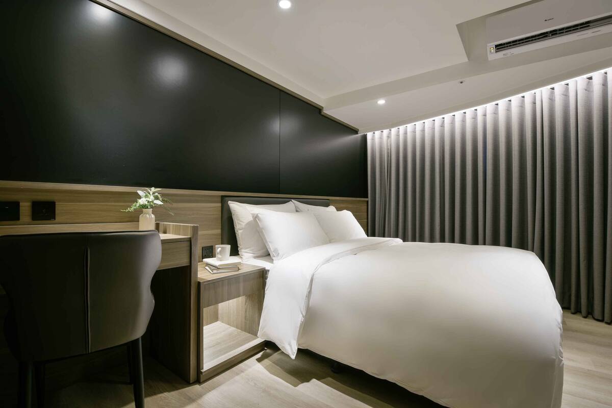 A modern hotel room with a bed, a desk, and a chair.