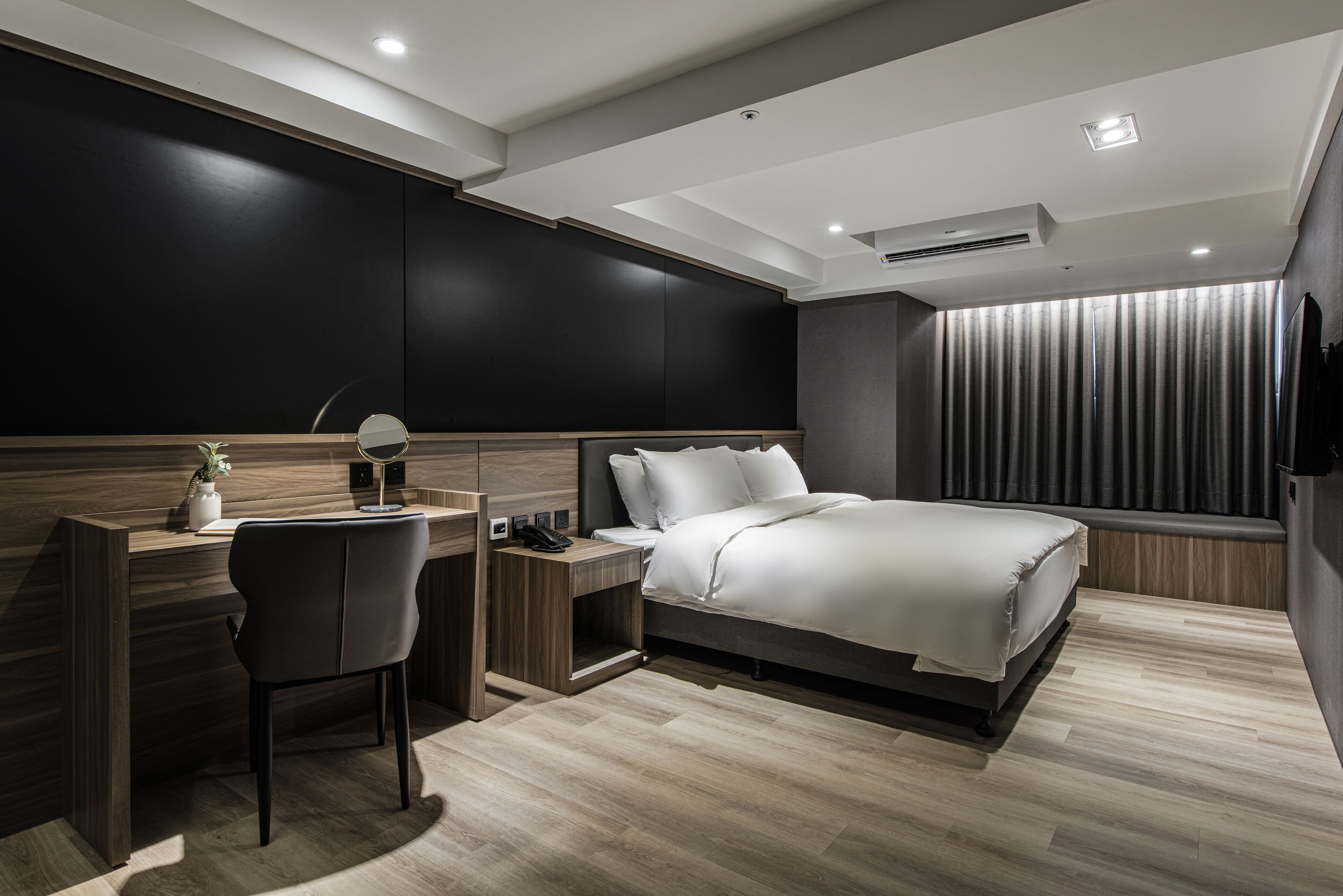 A modern hotel room with a bed, desk, chair, and a large window with curtains.