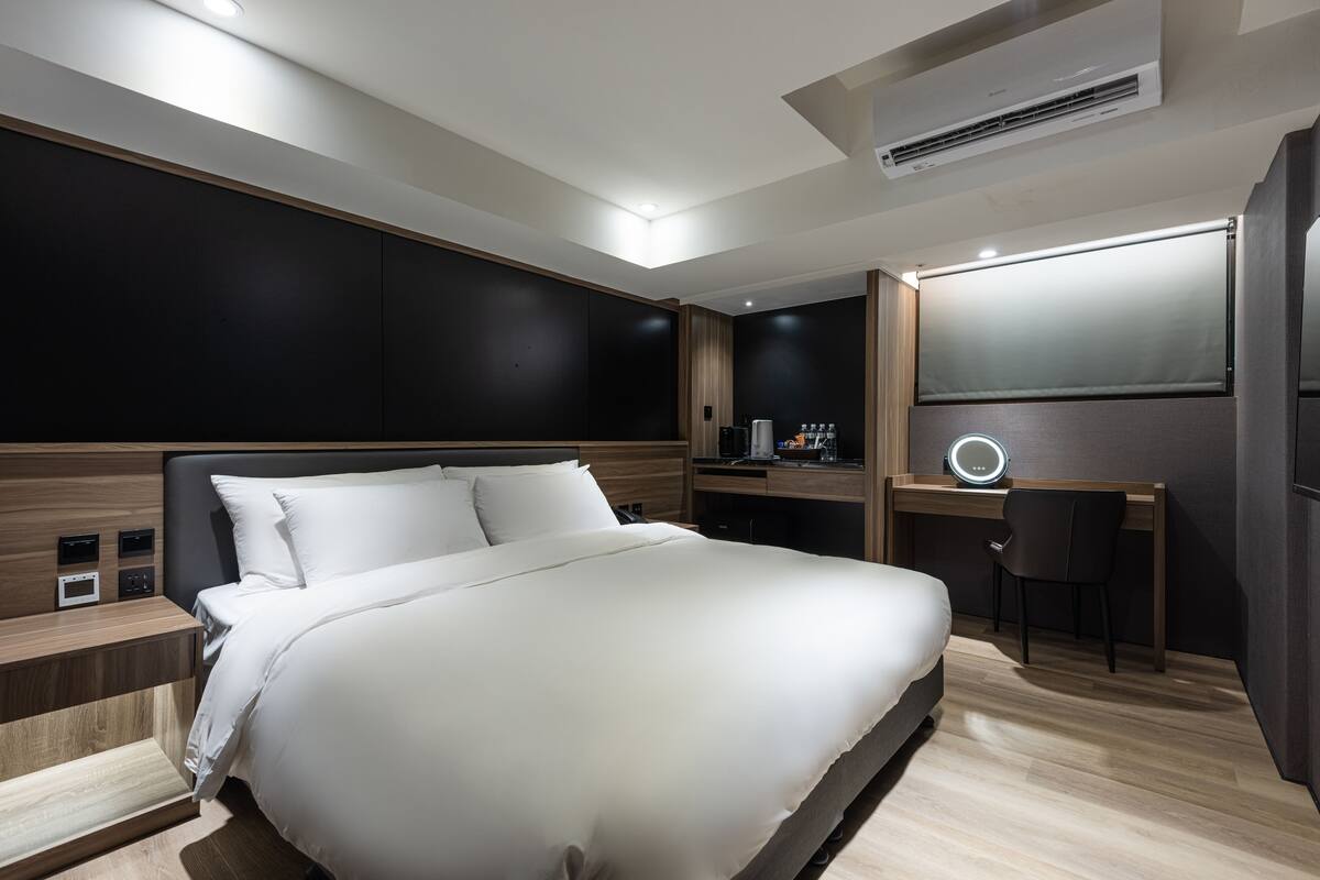 A modern hotel room with a large bed, a desk, a chair, and a large mirror.