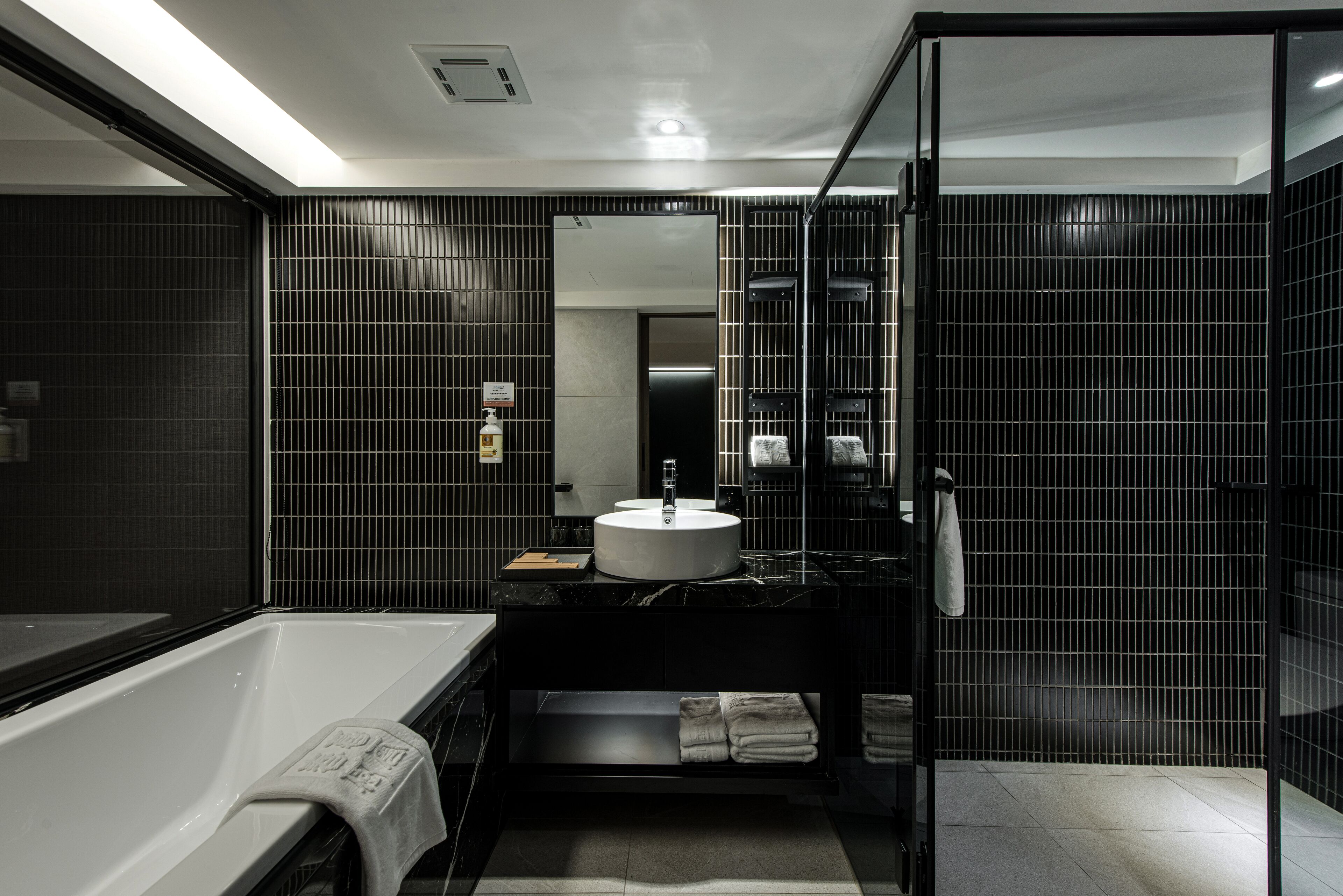 Un bany modern amb una banyera blanca, un lavabo negre amb un rentapel obert i una cabina de dutxa de vidre.