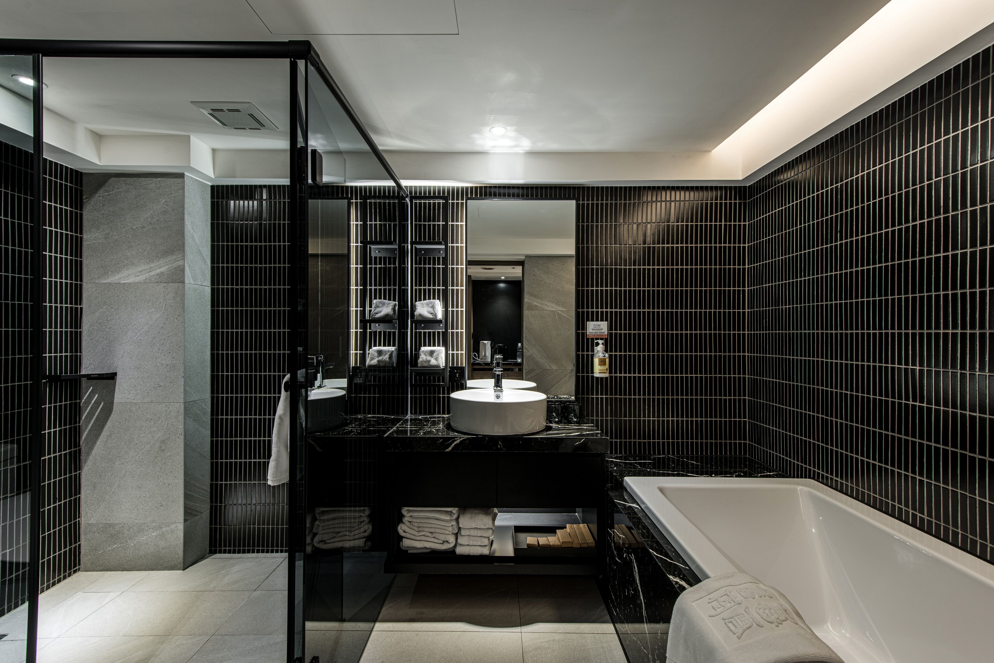 A modern bathroom with a black tiled wall, a white sink, and a bathtub.