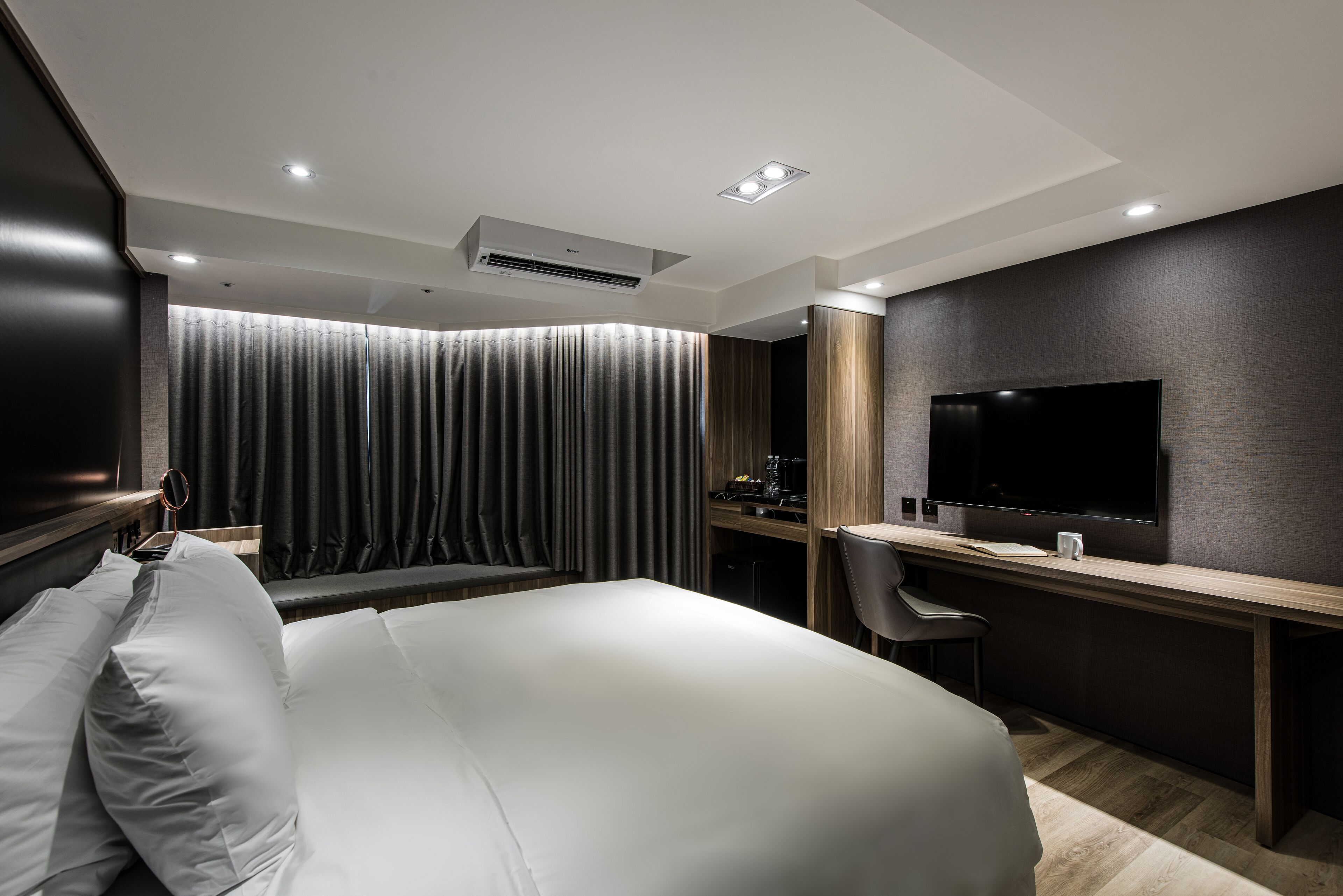 A modern hotel room with a large bed, a desk, a flat-screen TV, and a large window with curtains.
