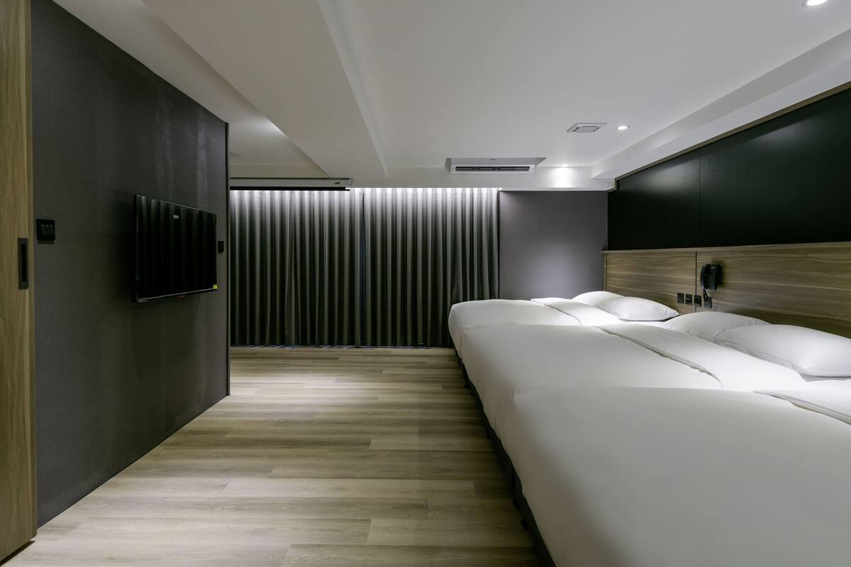 A modern hotel room with a large bed, a flat-screen TV mounted on the wall, and a wooden headboard.