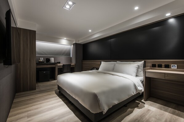 A modern hotel room with a large bed, a desk, and a built-in wardrobe.
