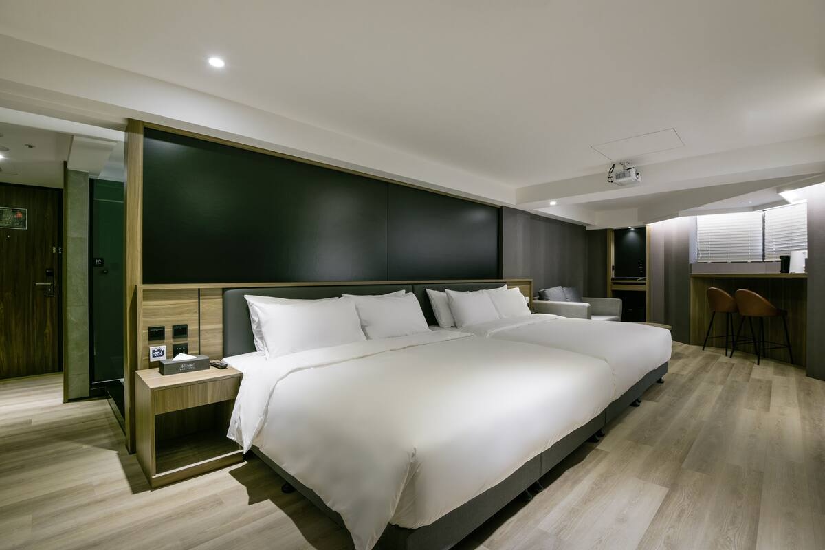A modern hotel room with a large bed, bedside tables, a desk, and a small kitchenette area.