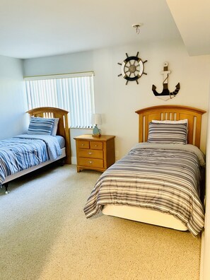 A bedroom with two single beds, a nightstand, a wall-mounted anchor decoration, and a window with blinds.