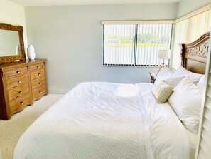 A bedroom with a large bed, a wooden dresser, a mirror, and a window with blinds.