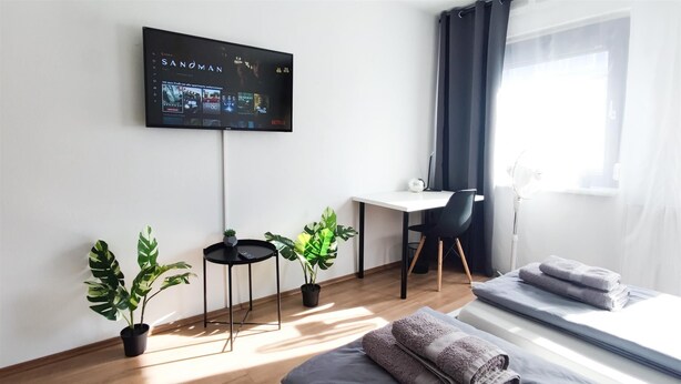 A modern hotel room with a bed, a desk, a chair, and a TV mounted on the wall.