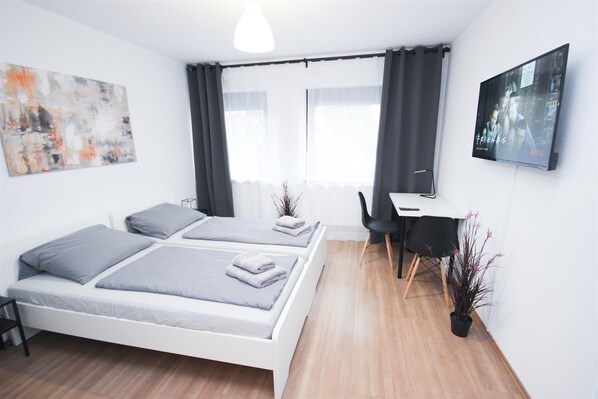 Una habitación de hotel moderna con dos camas individuales, un escritorio, una silla, un televisor y una ventana con cortinas.