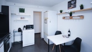 A compact kitchen with a microwave, coffee maker, and a small refrigerator. There is a dining table with chairs and a wine bottle on it.