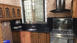 A kitchen with wooden cabinets, a stainless steel stove, and a window with metal bars. - C4 Mirpur City AJK Overseas Pakistanis Villa 3bed Guesthouse (Mirpur city AJK)