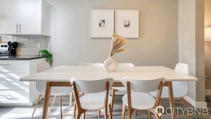Ein moderner Essbereich mit einem weißen Tisch, vier Stühlen und einer Vase mit Trockenpflanzen.