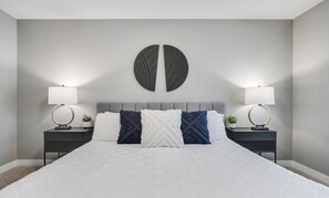 A neatly made bed with a white duvet, two bedside tables with lamps, and a wall-mounted circular decoration. - Westwood.Sleeps 8 - Central - A/C (Edmonton)